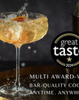 Cocktail glass with ice and a splash, next to a cocktail shaker, on a dark background with 'Great Taste' logo.