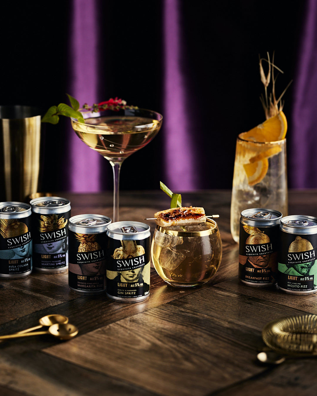 Cocktails with garnishes and SWISH cans on a wooden surface with a dark background