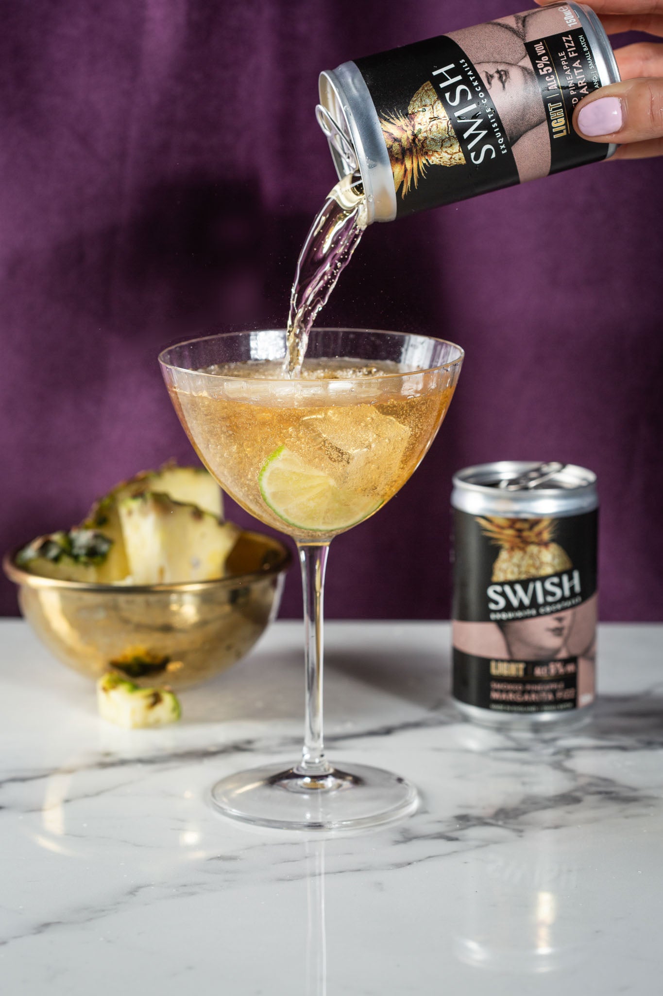 Pouring a canned margarita into a cocktail glass on a marble table